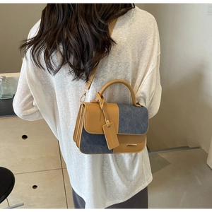 Detail of contrast stitch handbag with khaki leather and blue denim texture on model