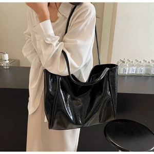 Detail of a large black glossy tote bag with slim shoulder straps in a minimalist setting