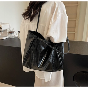 Glossy black large capacity tote bag shown on model in a stylish cafe setting