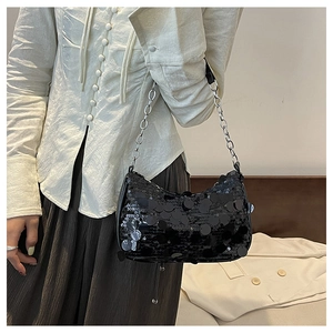 Detail of stylish black sequin underarm bag with silver chain strap worn by a model