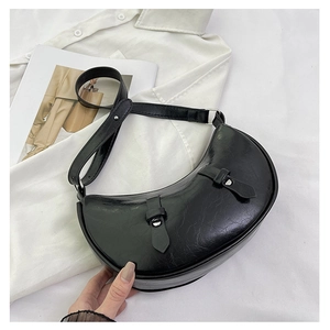 Detail of black crescent shoulder bag featuring glossy crinkled texture and silver buckles