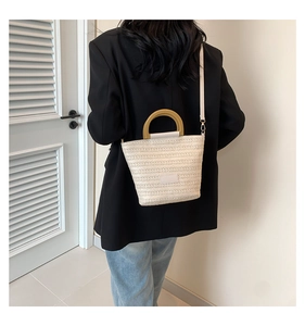 Detail of beige woven straw bucket bag with wooden handle and slim leather crossbody strap