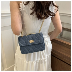 Blue denim quilted chain bag with gold metal clasp shown on a shoulder in a stylish setting