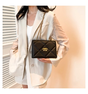 Classic black quilted chain shoulder bag with gold metal hardware on cream blazer