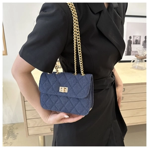 Détail d'un sac bandoulière en denim bleu matelassé avec chaîne dorée sur un mannequin