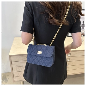 Detail of blue denim quilted crossbody bag with gold chain strap and metal turn lock