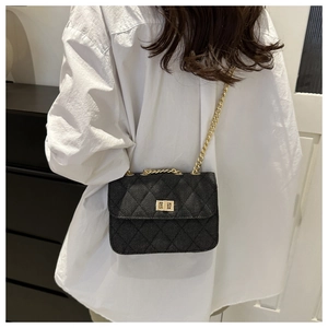 Détail du sac bandoulière en denim noir matelassé avec chaîne dorée sur chemise