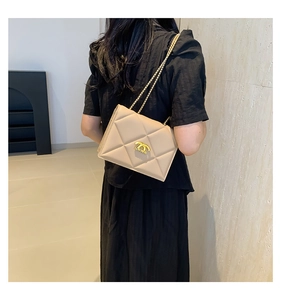 Detailed view of beige quilted chain bag with gold metal buckle on black clothing