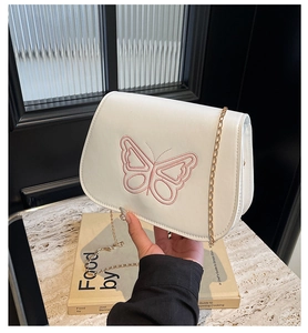Détail de la broderie papillon rose sur un sac à bandoulière beige à rabat
