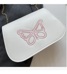 Détail d'un sac bandoulière blanc en similicuir avec broderie papillon rose et chaîne dorée