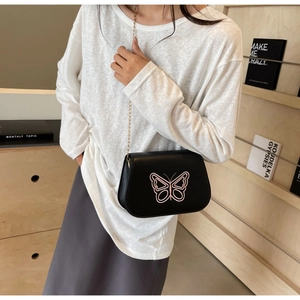 Détail du sac selle en cuir noir avec broderie papillon rose et bandoulière chaîne dorée