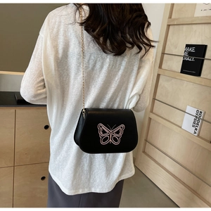 Détail du sac de selle en cuir noir avec broderie papillon rose et chaîne dorée chic