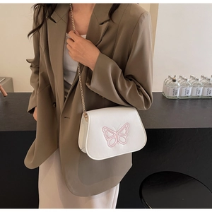 Détail du sac selle en cuir blanc avec broderie papillon rose et bandoulière dorée