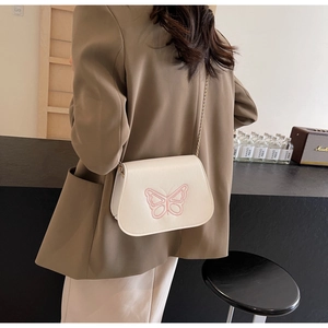 Détail d'un sac bandoulière blanc crème avec broderie papillon rose et chaîne dorée