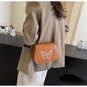 Détail du sac selle marron avec broderie papillon blanche et fine bandoulière chaîne dorée