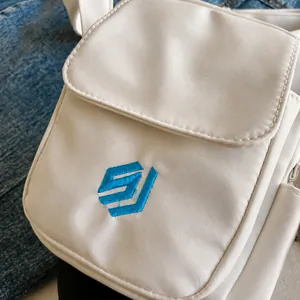Close-up of white canvas crossbody bag featuring detailed blue embroidery and woven texture