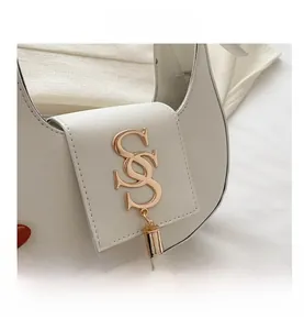 Gros plan d'un sac demi-lune blanc avec texture cuir et logo SS doré et pompon chic