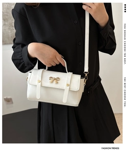 Detail of white mini crossbody bag with gold bow lock on black shirt dress background