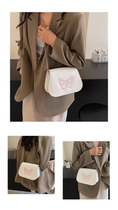 Détail du sac selle blanc avec broderie papillon rose et bandoulière chaîne dorée