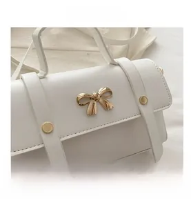 Close-up of white leather handbag featuring a golden bow-knot buckle and metal rivets