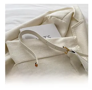 Détail du sac bandoulière en cuir blanc cassé avec boucle dorée et logo élégant