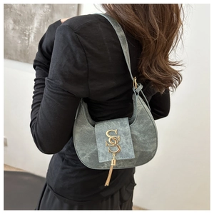 Détail du sac croissant gris avec logo SS doré et pompon porté par un mannequin
