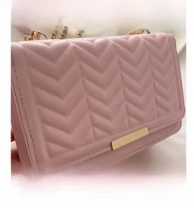 Close-up of pink quilted small square bag with V-stitch texture and gold metal chain strap
