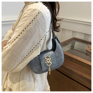 Détail du sac hobo en denim bleu avec boucle S dorée et pompon en métal sur un mannequin