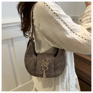 Détail du sac demi-lune marron avec texture mate et breloque logo S métallique élégante