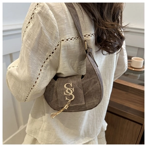Détail du sac hobo marron vintage avec logo en métal doré et pompon sur le mannequin