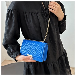 Detail of royal blue quilted crossbody bag with gold chain strap and V-shaped stitching