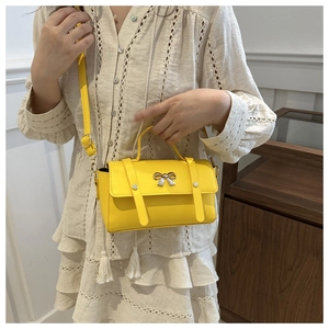 Detail of yellow crossbody bag with silver bow accent and adjustable shoulder strap