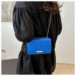 Detail of blue quilted crossbody bag featuring chevron stitching and gold chain strap