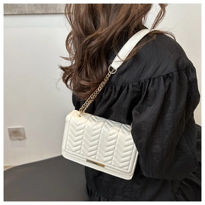 Detail of white quilted crossbody bag featuring V-shaped stitching and gold chain strap