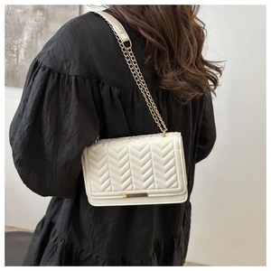 Detailed view of a white quilted shoulder bag with gold chain strap and V-pattern texture