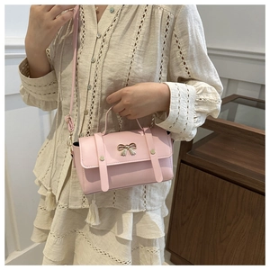 Close-up of light pink crossbody bag with metal bow detail and adjustable strap on model