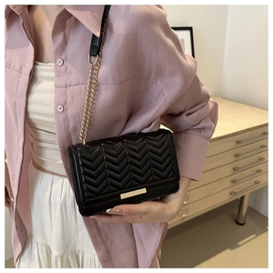 Detail of black V-quilted crossbody bag with gold chain strap worn on pink shirt