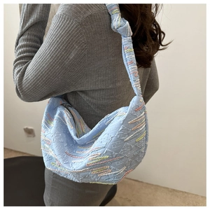 Detail of light blue shoulder bag with unique textured 3D pleats and wavy colorful embroidery