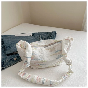 Detail of white quilted dumpling bag with colorful embroidery and a knotted strap
