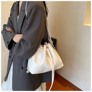 Detailansicht einer weißen Beuteltasche an einem Model mit grauem Blazer und Faltenrock