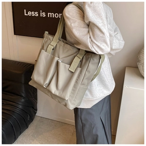 Detail view of khaki nylon tote bag featuring front utility pockets and a woven strap
