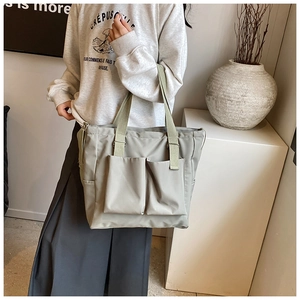 Detail of grey-green nylon tote bag featuring functional dual front pockets and wide straps