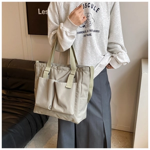 Detail of sage green nylon tote bag with double front utility pockets and long straps