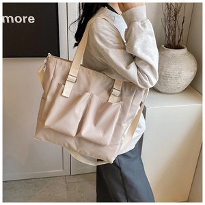 Detail of beige nylon tote bag with front pockets and adjustable strap on a model