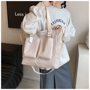 Detail of beige nylon tote bag featuring front utility pockets and adjustable shoulder strap