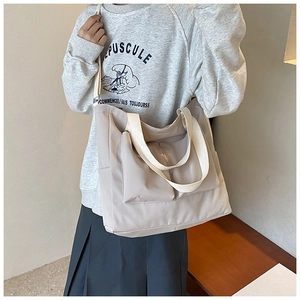 Close-up of beige nylon tote bag featuring two large front flap pockets and wide shoulder strap
