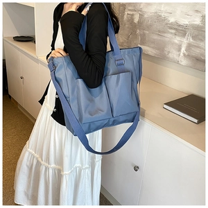 Detailed view of blue nylon tote bag showing front pockets and adjustable shoulder strap