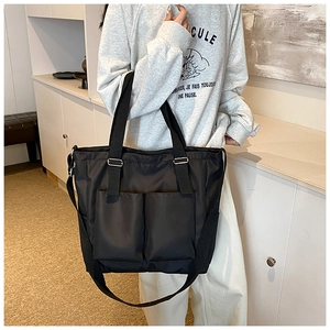 Detail of black nylon tote bag featuring double front pockets and adjustable strap