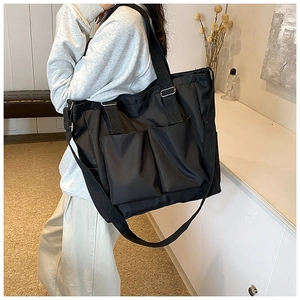 Detail of black nylon tote bag featuring functional front pockets and adjustable crossbody strap