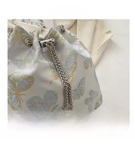 Close-up of light blue silk bucket bag featuring butterfly embroidery and pearl pendants